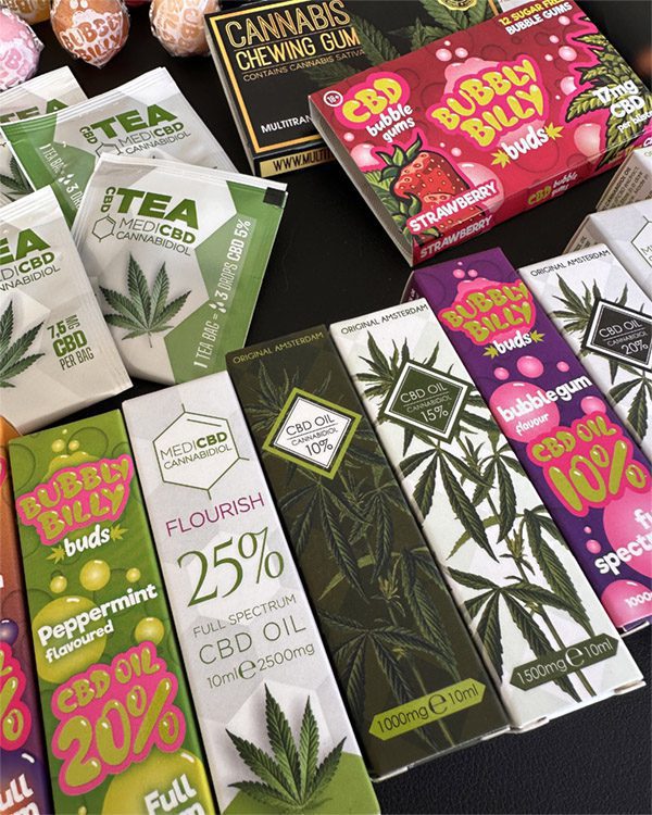 A variety of CBD products including teas, oils, chewing gum, and lollipops displayed on a black surface.