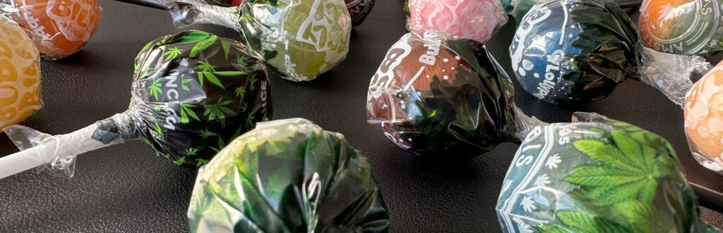 Green-wrapped cannabis lollipops displayed in a row, showcasing Amsterdam's iconic edible souvenir.